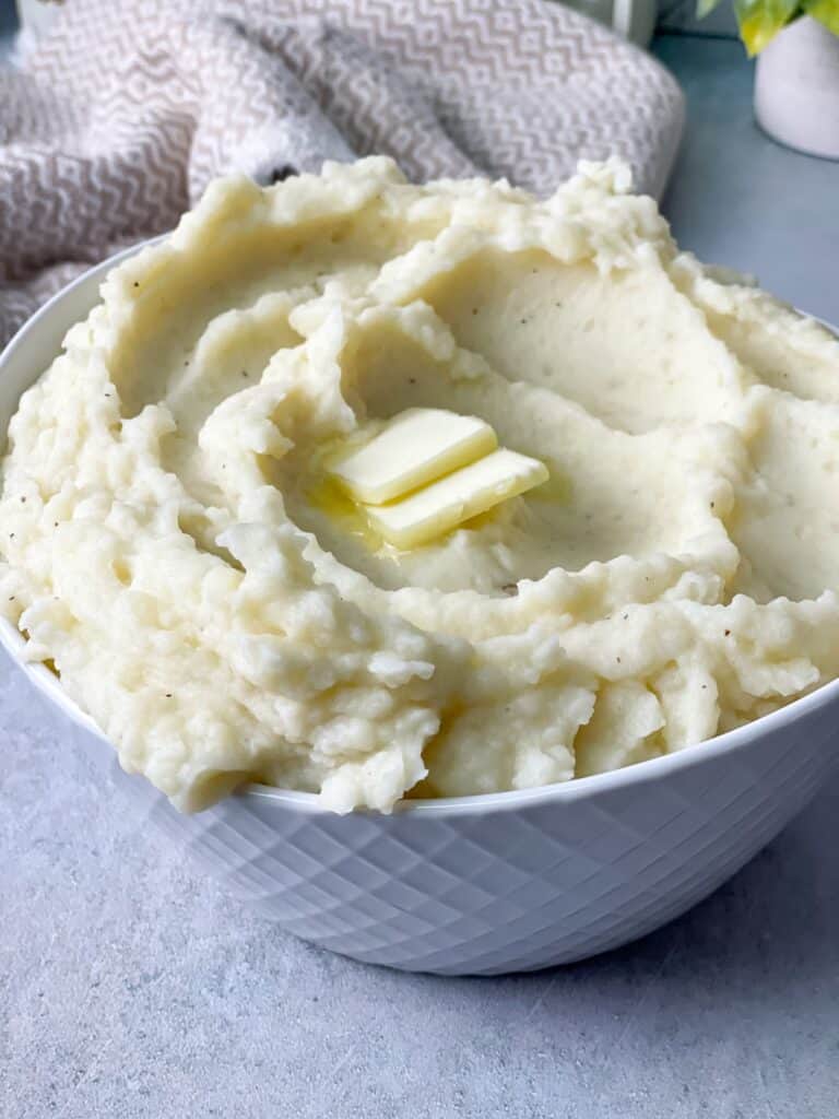 a close up shot of creamy mashed potatoes bowl with pieces of butter