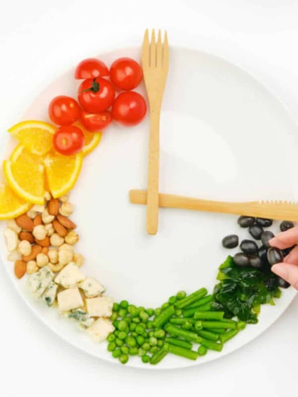 Colorful food and cutlery are arranged in the form of a clock on a plate.