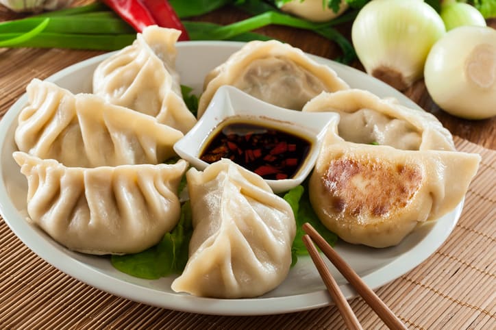 a small bowl of dumpling dipping sauce in the middle of a plate of freshly cooked dumplings