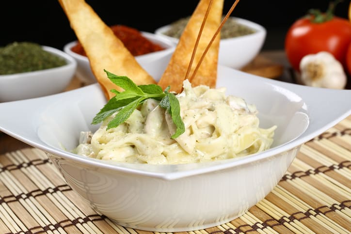 A creamy fettuccine Alfredo decorated on top with mint and bread. Next to tomatoes and garlic.