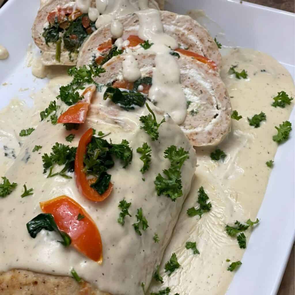 tasty chicken roulade with white sauce on top and garnished with fresh parsley