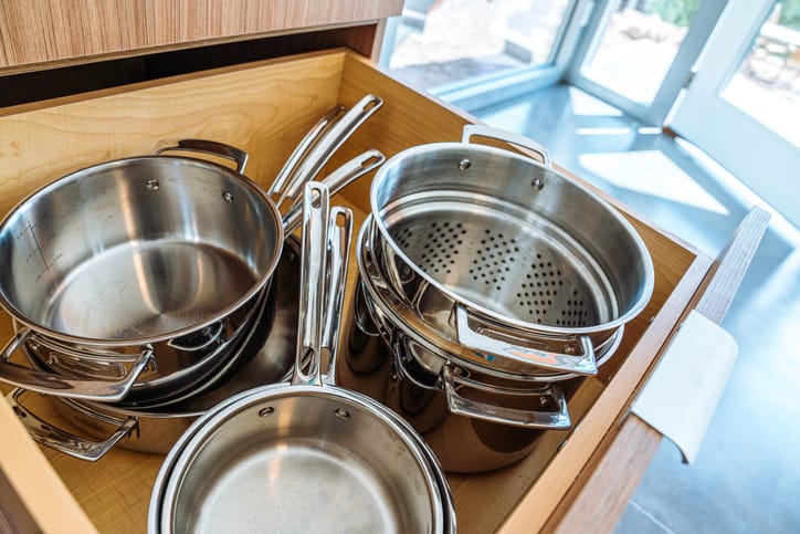 Close-Up Shot of Stainless Steel Pots and Pans in a Wooden Drawer in a Trendy Kitchen