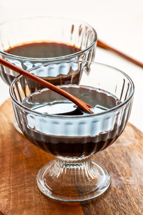 two glass cups contain homemade organic black cane molasses placed on a wooden table