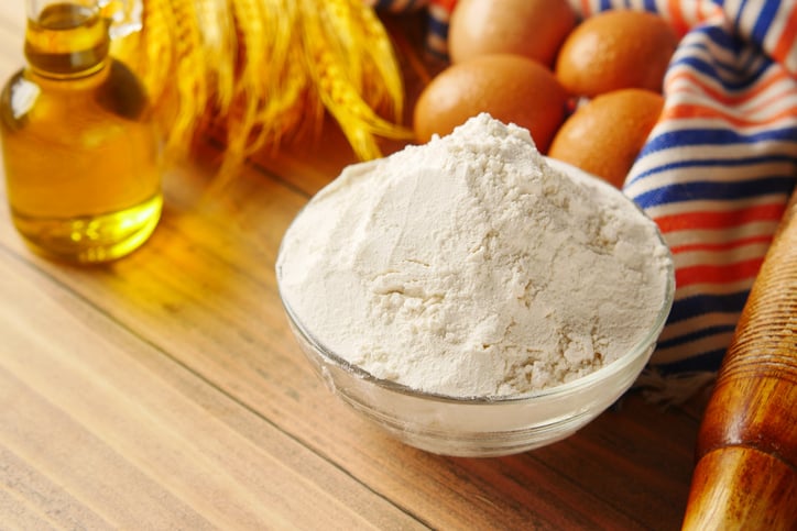 self-rising flour in a glass bowl on table alongside vegetable oil and eggs