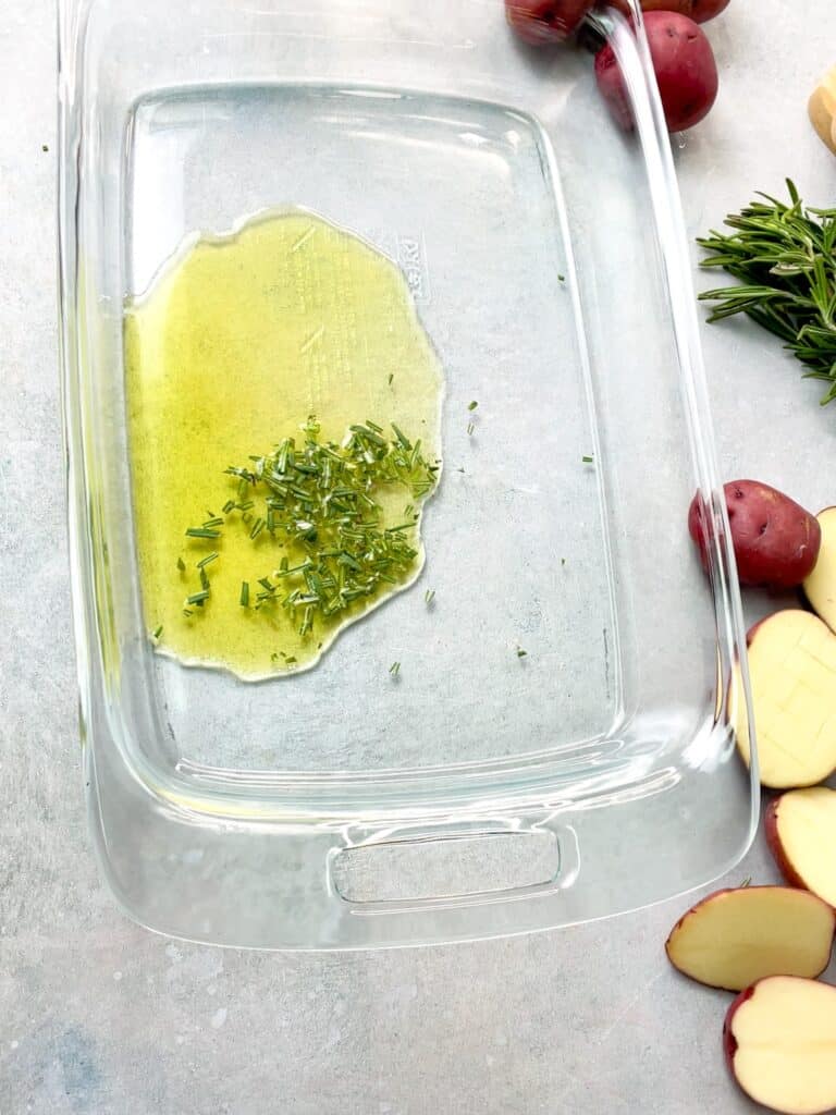 a baking dish with some olive oil and finely chopped rosemary
