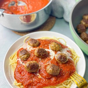 a white plate of spaghetti sauce topped with white tomato sauce and meatballs