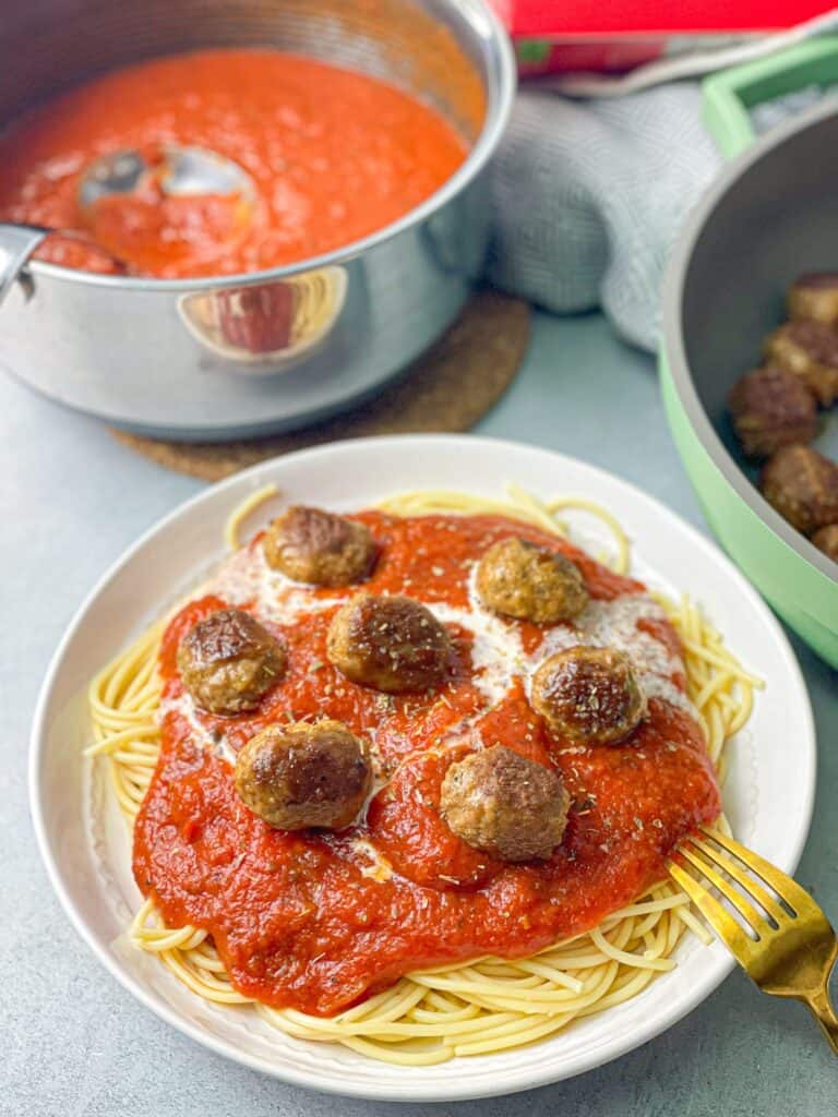 a white plate of spaghetti sauce topped with white tomato sauce and meatballs