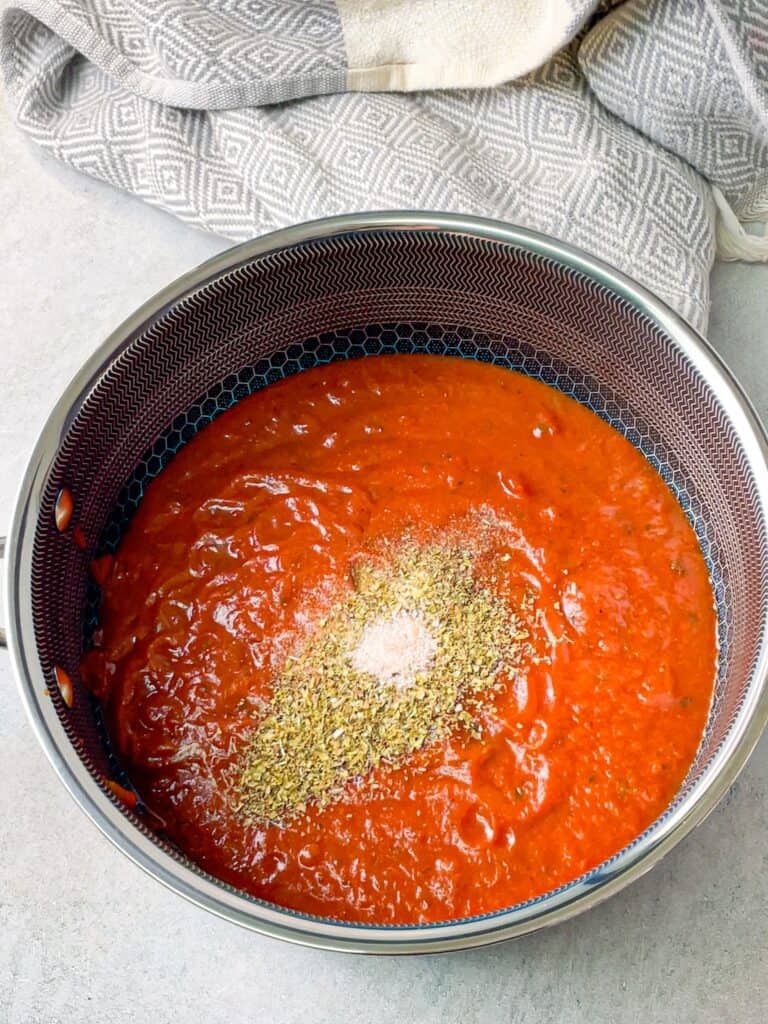 a sauce pan filled with jarred pasta sauce seasoned with some spices