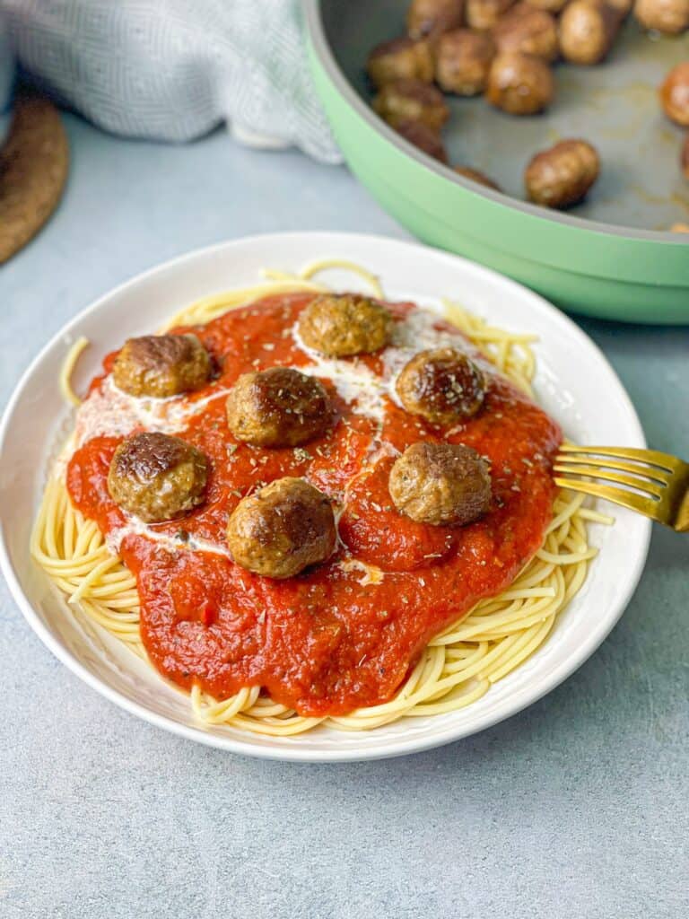 a white plate of spaghetti topped with pasta sauce ad brown meatballs