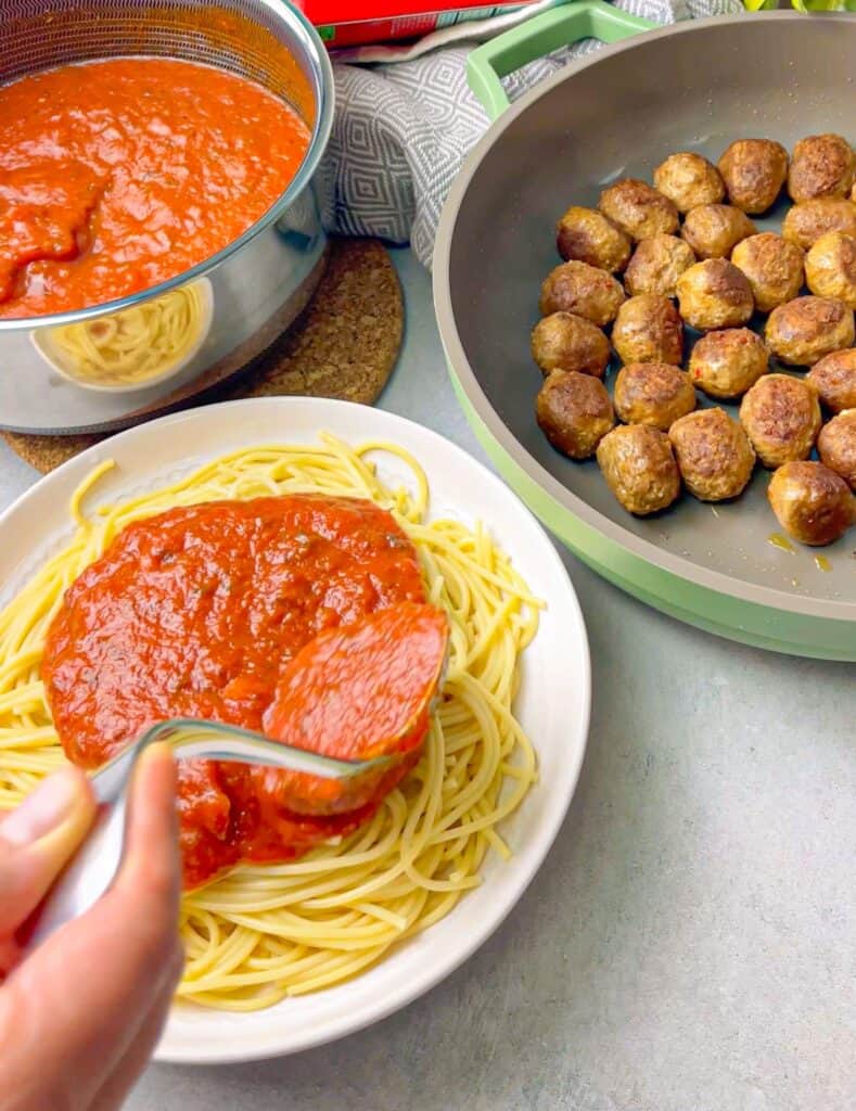 a white dish of spaghetti with pasta sauce drizzled on top