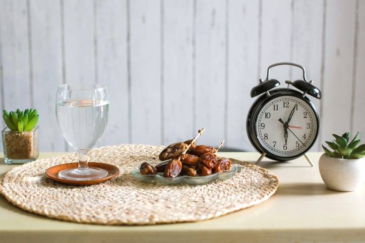 Glass of water and dates with alarm clock showing 6 o'clock. Traditional Ramadan, iftar time concept