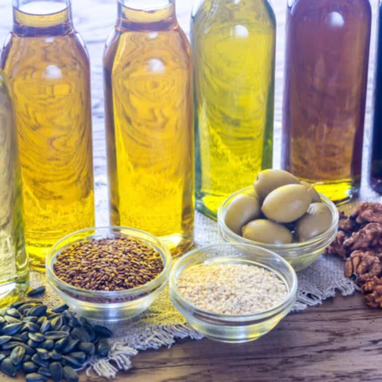 Different types of oils in glass bottles next to their natural source.