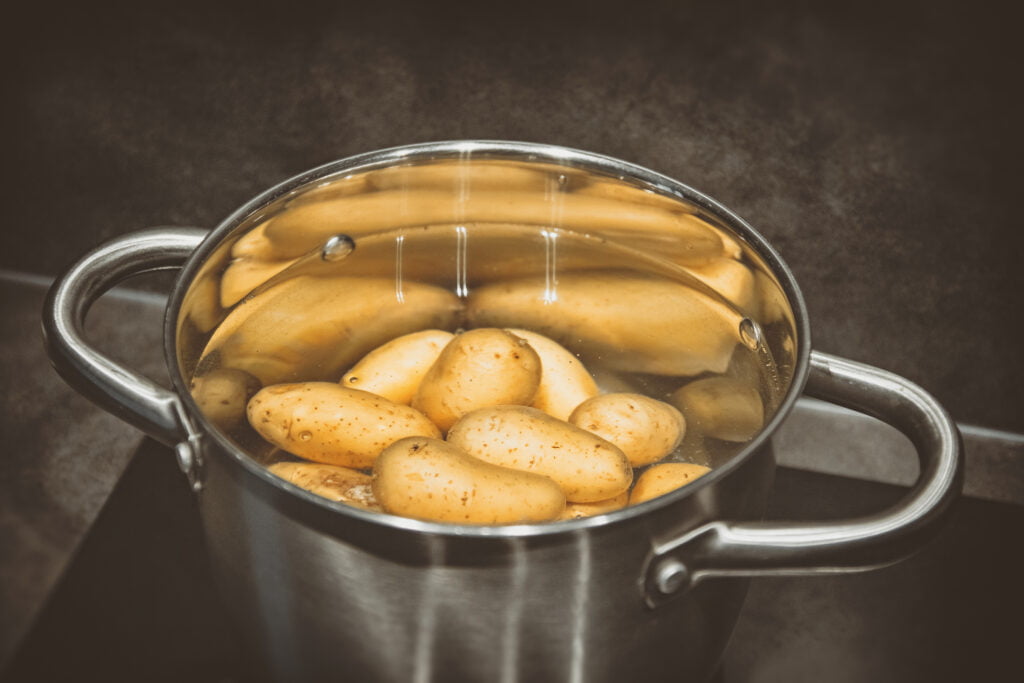 Raw whole potatoes submerged in water in a metal pot, ready for boiling