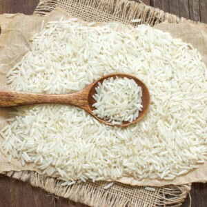 A stack of white basmati rice with a wooden spoon in the middle filled with white basmati rice.