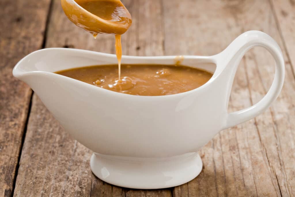 a small white ladle pouring au jus substitute which is a brown gravy into a white ceramic gravy boat.