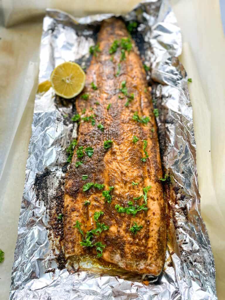 perfectly baked blackened salmon on foil with a crusty brown skin garnished with parsley
