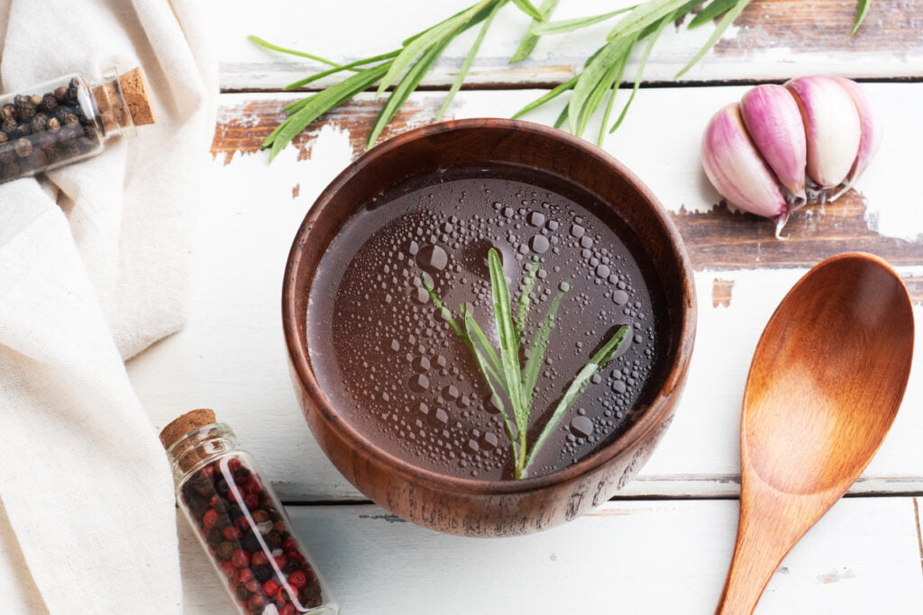 boiled meat broth in a wooden bowl with garlic, black pepper, and rosemary