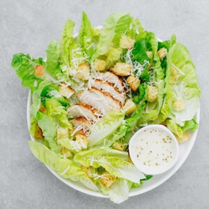 a top view of Caesar salad, with romaine lettuce hearts, croutons, parmesan cheese, and homemade Caesar salad dressing