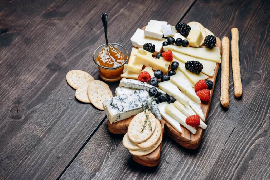 various types of cheese are served with berries and crackers on a wooden board