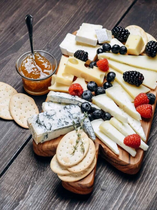 different types of cheese are served with berries and crackers on a wooden charcuterie board
