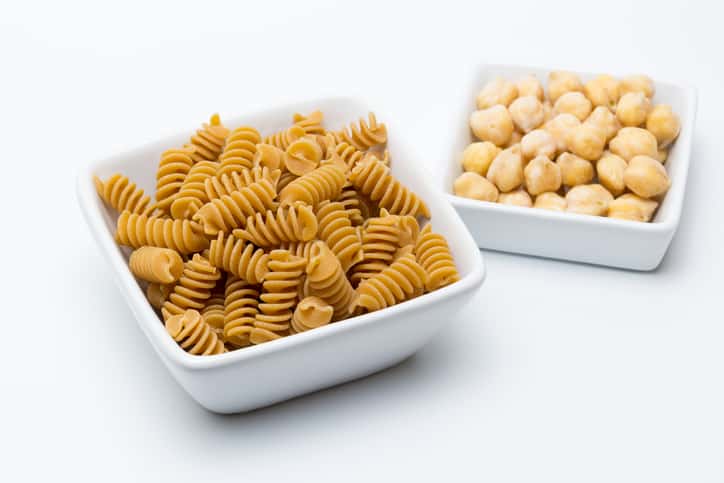 Two ceramic pots are placed next to each other. One contains uncooked pasta while the other contains healthy raw chickpeas.
