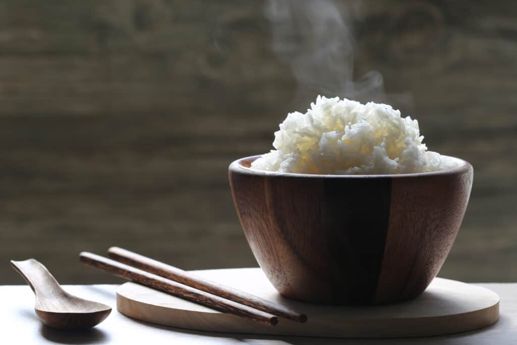 Cooked basmati rice in wooden bowl with smoke rising in the  background.