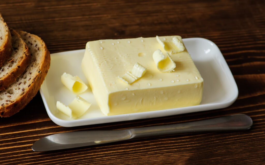 A piece of butter with knife and bread on a wooden desk
