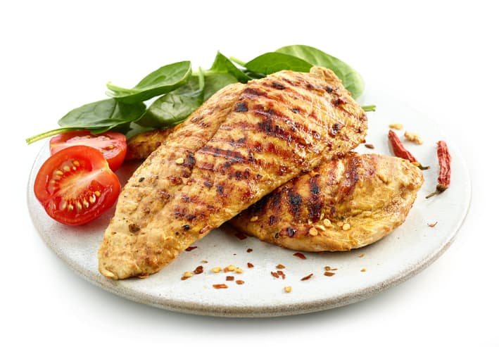 tender juicy chicken fillet served on white plate alongside fresh tomato, fresh basil leaves, and red pepper