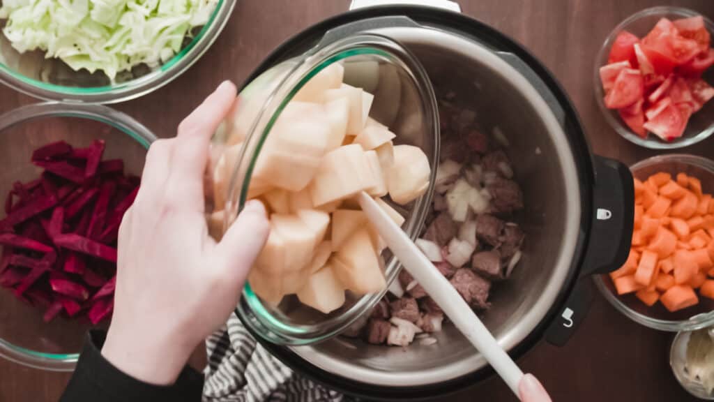 many glass bowls placed on a wooden counter contain freshly chopped veggies ready to be cooked in an instant pot