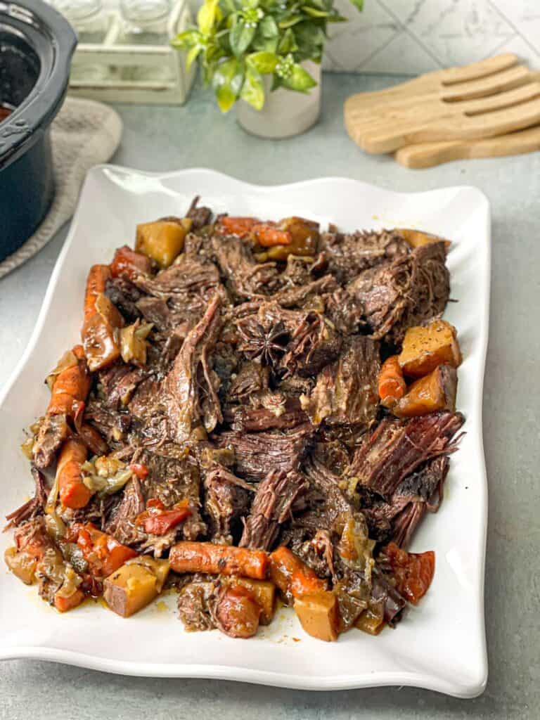a large plate of juicy tender slow cooker roast with tomato, carrots, onions, potatoes, and beef gravy