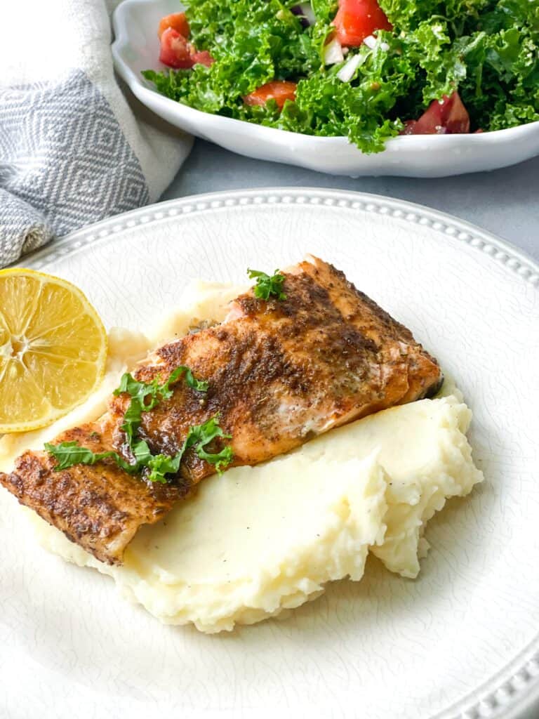 baked blackened salmon served on a bed of mashed potatoes and a bowl of salad