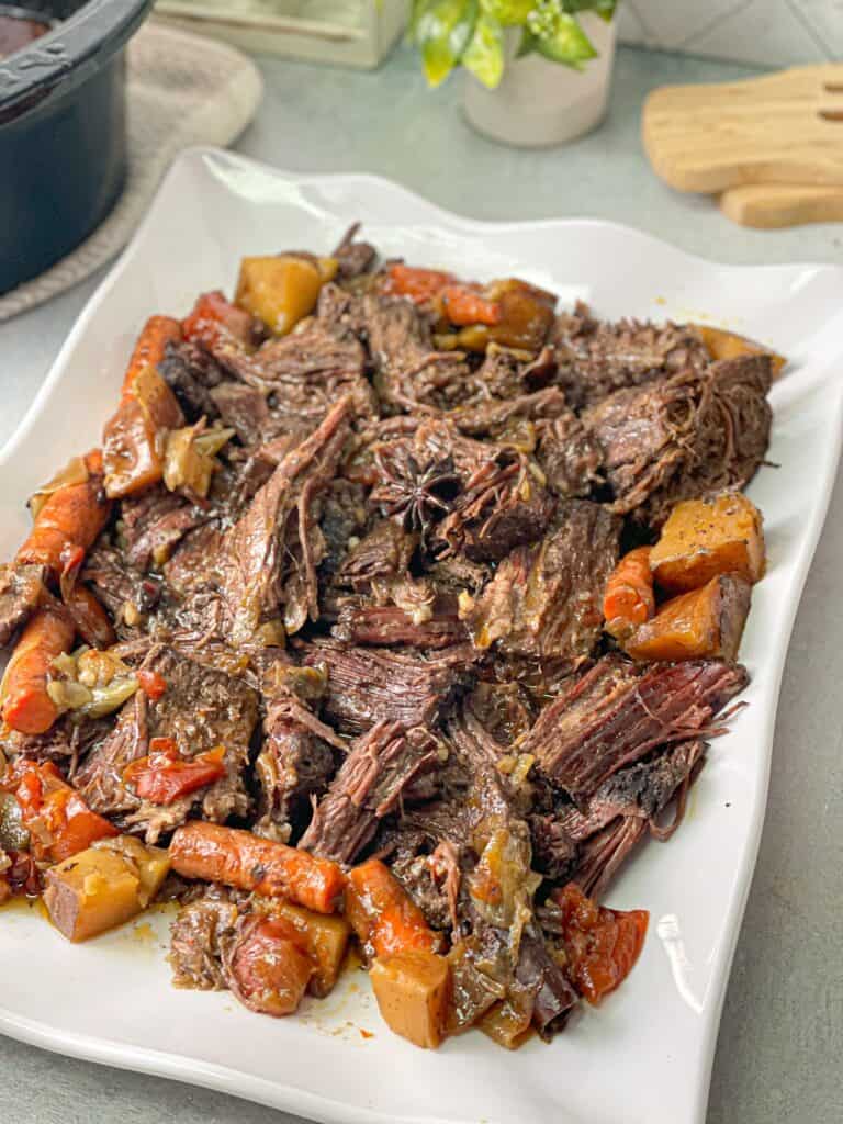 juicy cooked roast beef with beef gravy, tomato, carrots, onions, and potatoes served in a large plate 