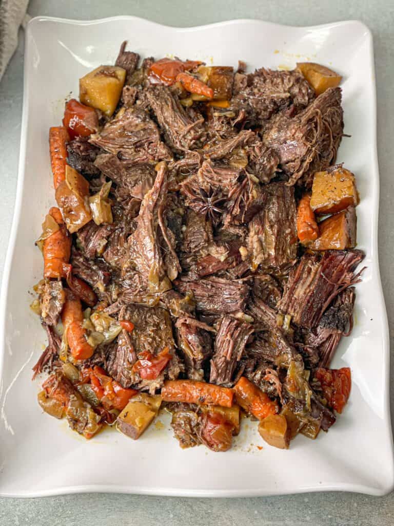 a large plate of juicy tender slow cooked roast beef with tomato, carrots, onions, and potatoes