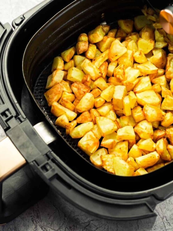 Small pieces of potatoes are being fried in the basket of an air fryer.