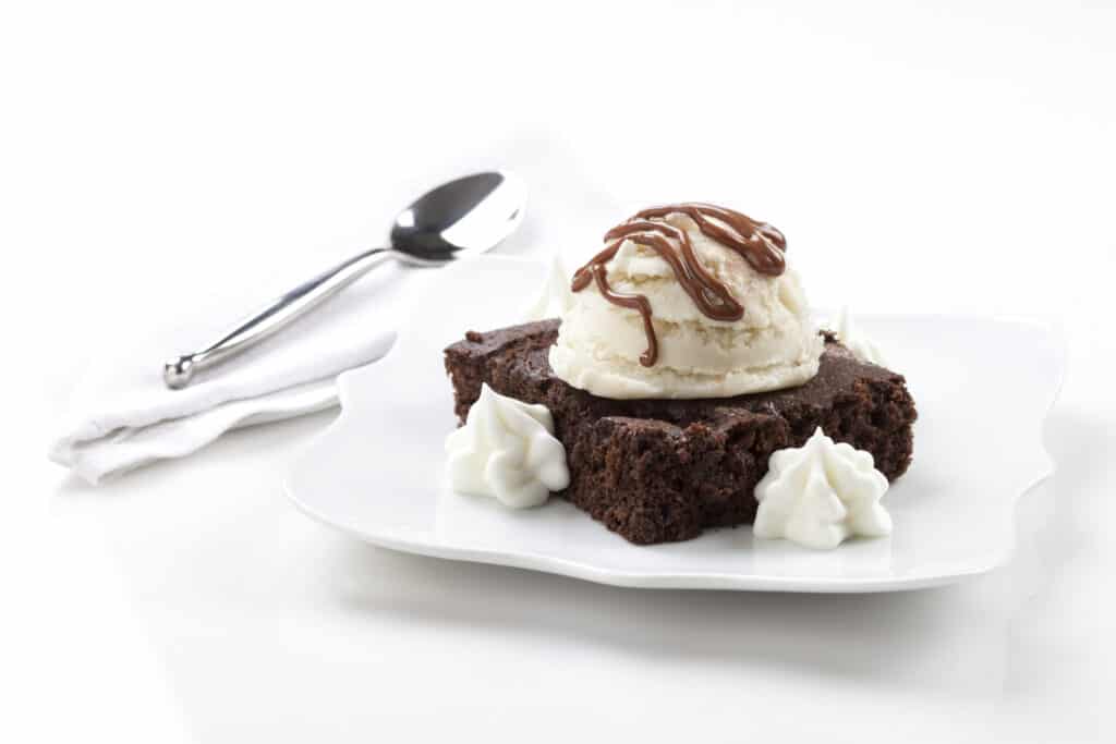 a fudgy brownie served with a scoop of vanilla ice cream and two dollops of whip cream and chocolate syrup drizzle