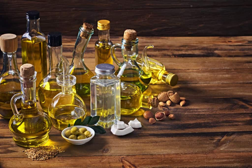 Assorted healthy vegetable oil bottle collection on wooden table in a old fashioned kitchen: Olive oil, hazelnut oil, almond oil, coconut oil and sesame oil