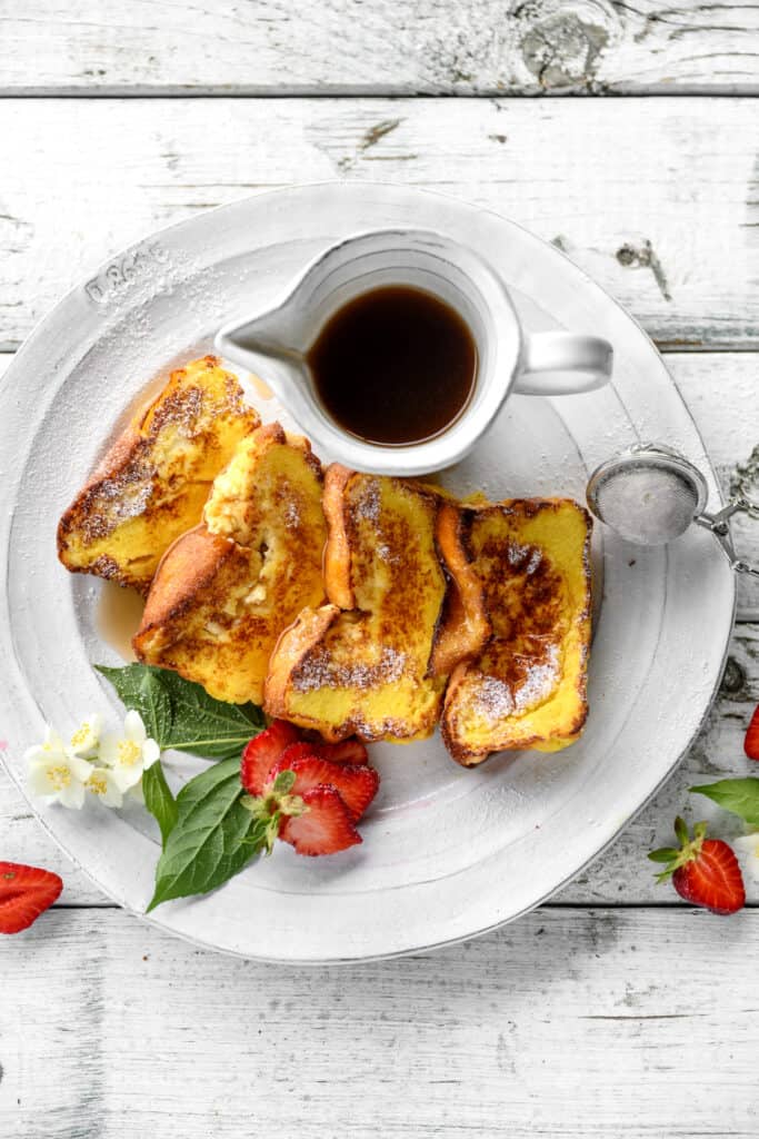 a dish with 4 French toast slices served with maple syrup and fresh strawberries