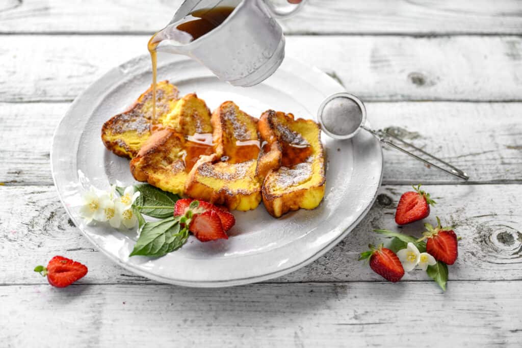 4 French toast slices drizzled with maple syrup and served with fresh strawberries