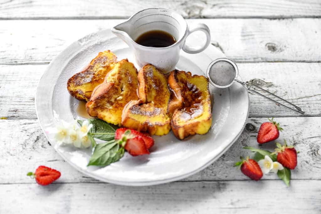 4 French toast slices drizzled with maple syrup and served with fresh strawberries