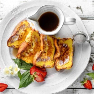 a top view of 4 French toast slices served with maple syrup and fresh strawberries