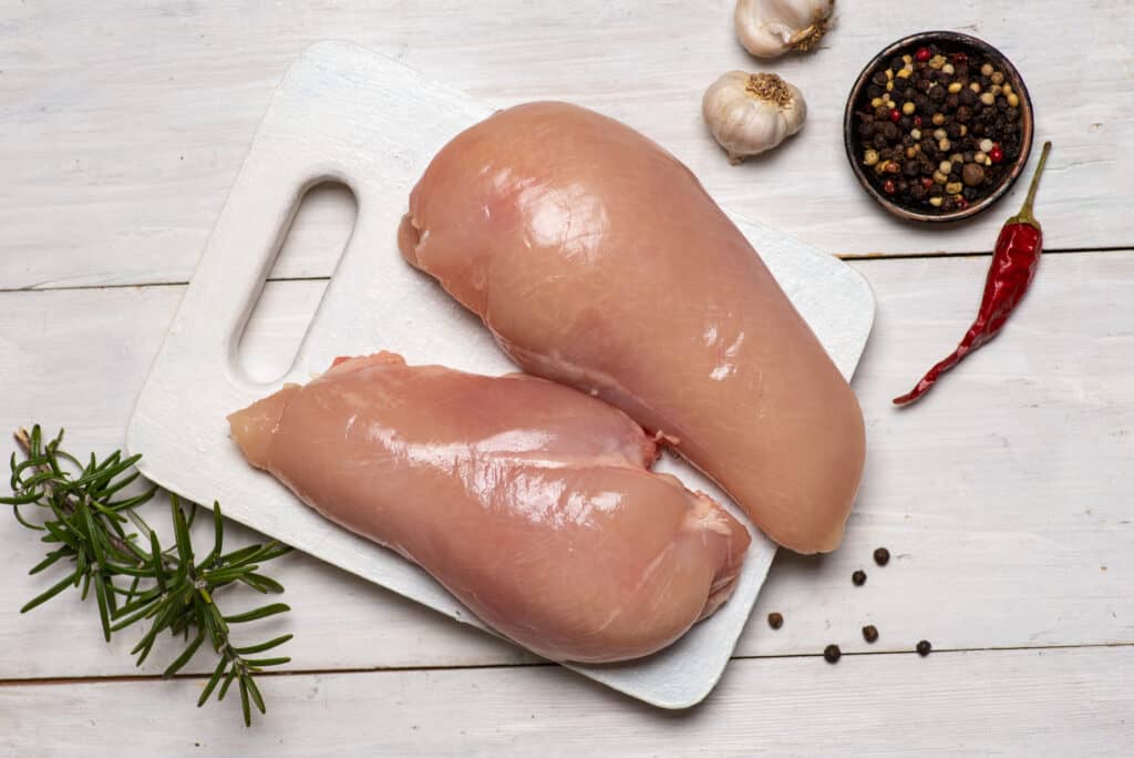 Raw uncooked deboned chicken breast with cooking ingredients on a wooden background