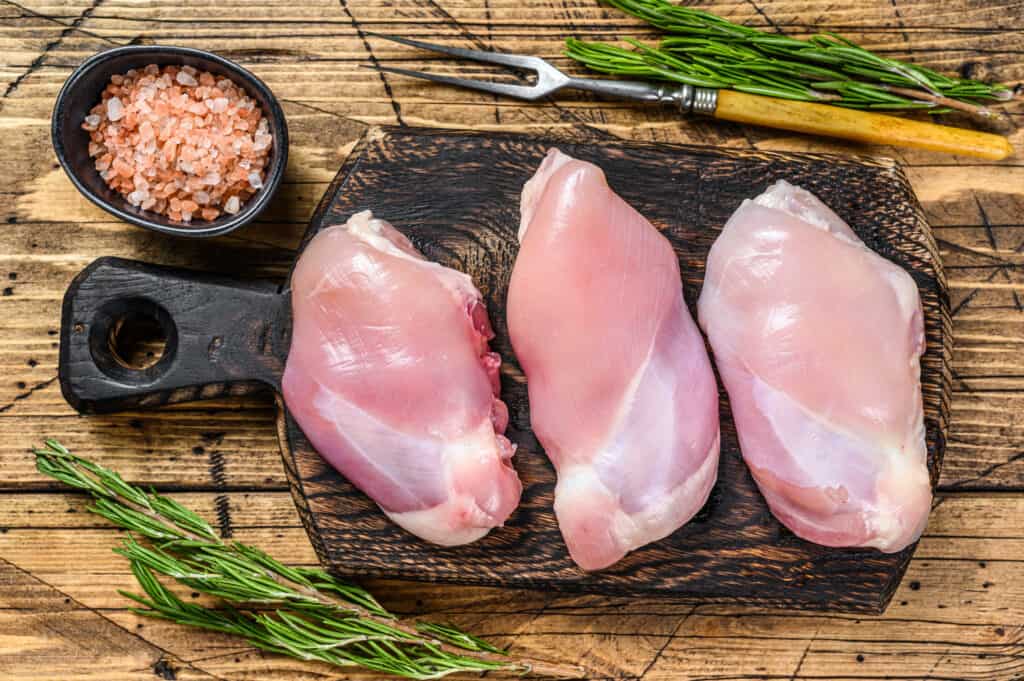 Boneless raw chicken is ready to be deboned on a wooden chopping board. Top view.