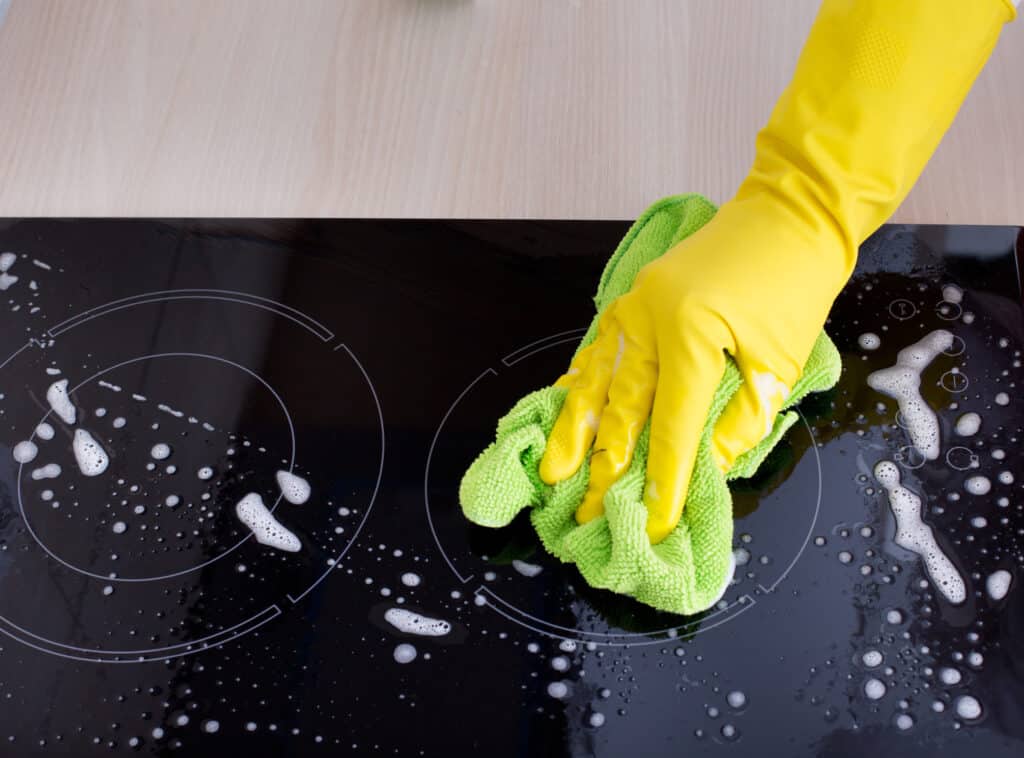 Close up of human hand with protective gloves cleaning electric stovetop with green mop