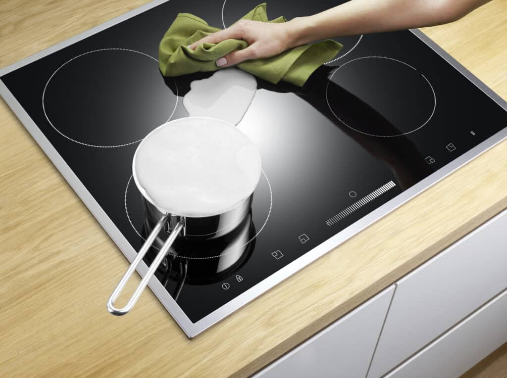 Wiping spills from a black electric stovetop with a clean green cloth