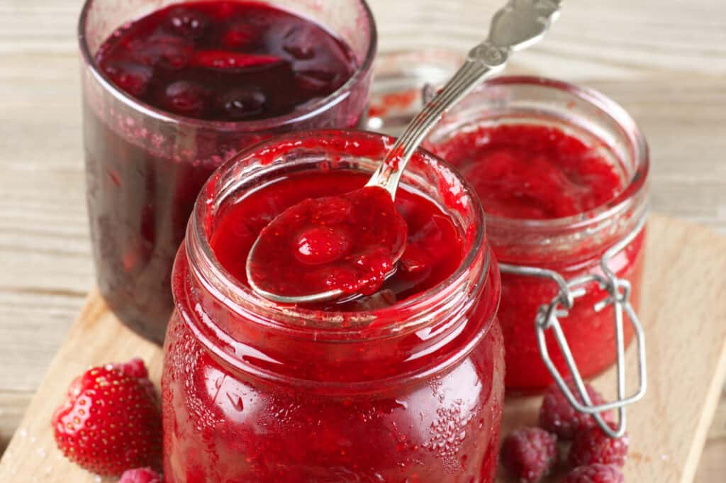 Assorted strawberry jam in glass jars. And a spoonful of glossy strawberry jam. 