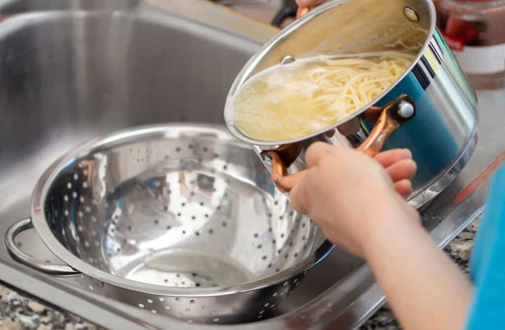 woman separating water from spaghetti with empty silver colander