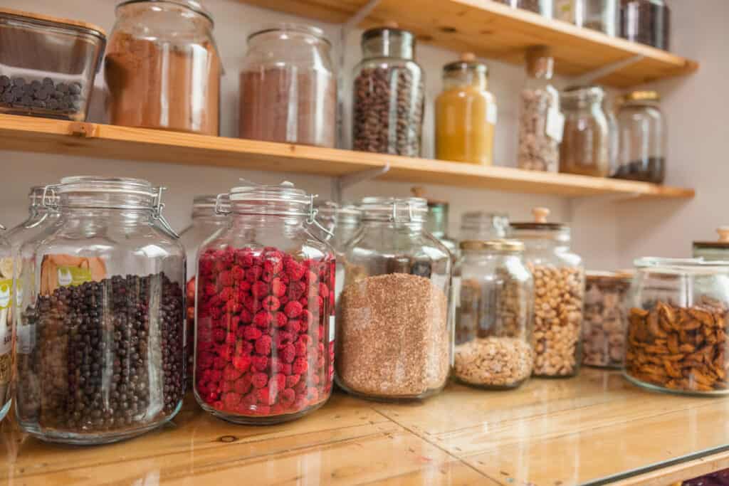 pantry shelves stacked with mason jars in different sizes that contain a variety of pantry staples, oats, dried fruits, spices, and chocolate chips.