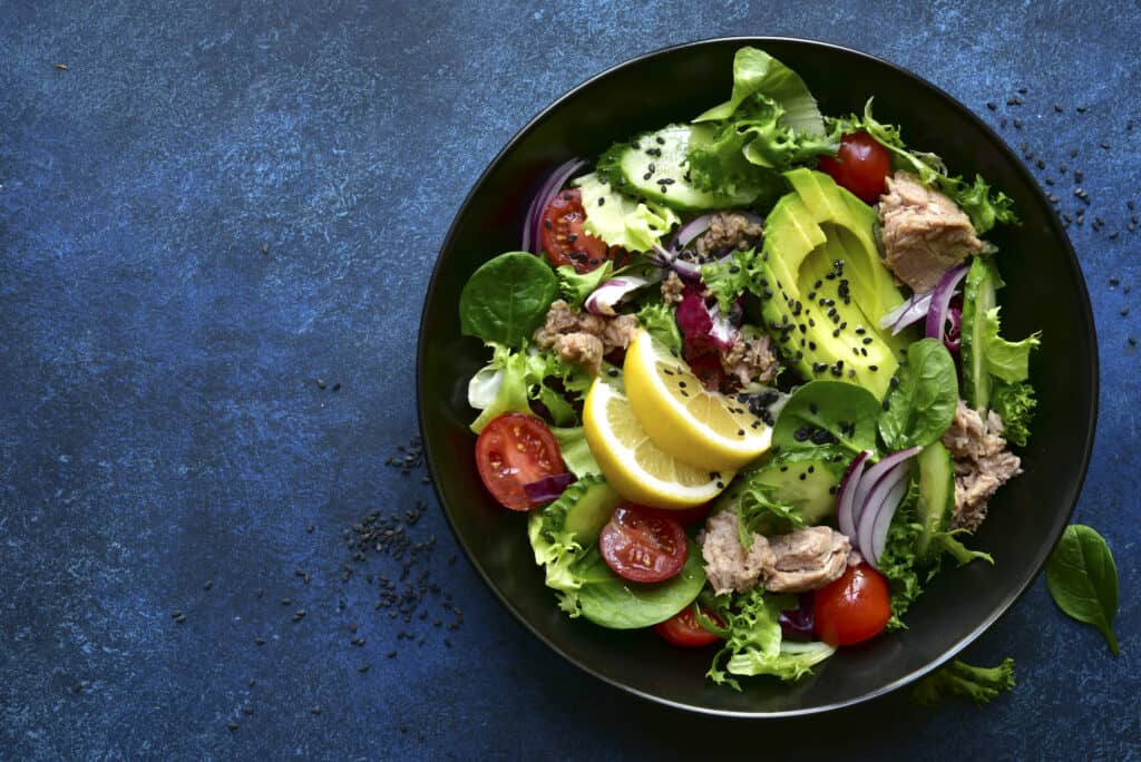 A tuna salad meal with avocados, slices of onions and lemons, chia seeds sparkles, lettuce and cherry tomatoes.