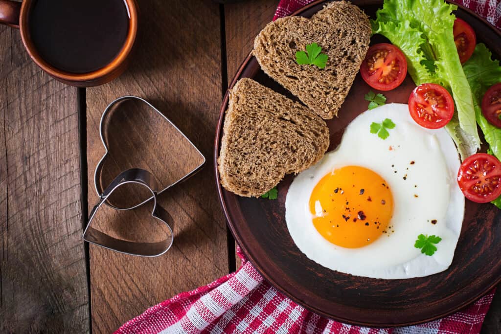 Breakfast ideas for newlywed - fried eggs and bread in the shape of a heart and fresh vegetables..