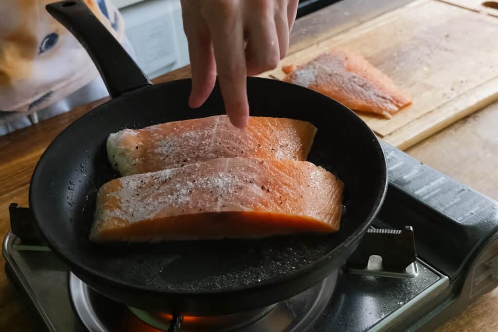 Two pieces of salmon being baked in a pan on a stove.